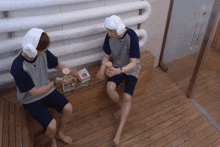 two men with towels on their heads are sitting on a wooden bench