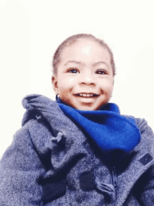 a young boy wearing a gray coat and a blue scarf smiles