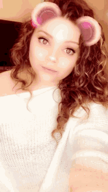 a woman with curly hair wearing a white sweater and pink ears on her face