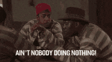 two prisoners are sitting at a table and one of them is saying " ain 't nobody doing nothing ! "