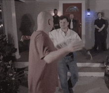 a bald man in a red shirt is standing next to another bald man in a white shirt