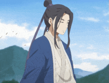 a man with long hair and a blue jacket stands in front of a mountain