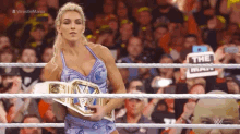 a woman is holding a wrestling championship belt in a ring