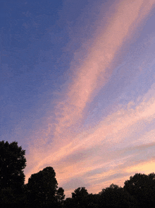 a sunset sky with trees in the foreground and a few clouds in the background