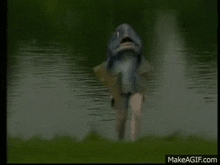 a fish is standing on the shore of a lake holding a fish in its mouth .