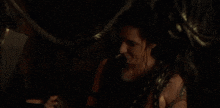a woman is sitting in a dark room with a rope around her neck and a ring on her finger .