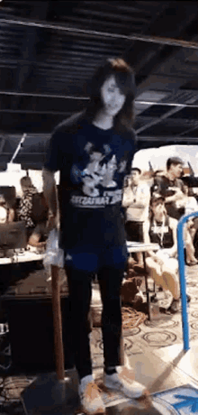 a man with long hair is standing in front of a crowd holding a shovel and a skateboard .