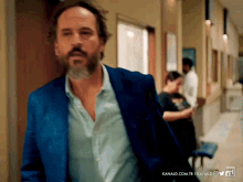 a man in a blue suit is walking down a hallway with kanald.com.tr in the lower right corner