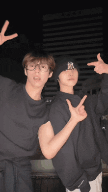 a man wearing a ny hat stands next to another man giving a peace sign