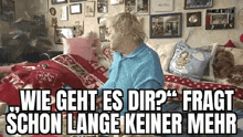 a woman in a blue sweater is sitting on a bed with a lot of pictures on the wall .