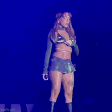 a woman in a green crop top and blue skirt is holding a microphone on a stage .