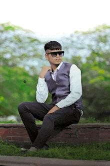 a young man wearing sunglasses is sitting on a brick wall