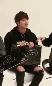 a young man in a black hoodie is sitting on a white chair holding a black box .