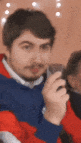 a man with a beard is holding a cell phone in his hand and looking at the camera .