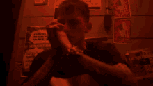 a man is smoking a cigarette in a dark room in front of a wall with posters on it .
