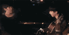 a man is playing a guitar in front of another man in a dark room .