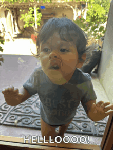 a baby standing in front of a glass door with the words hellooo on it