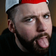 a man with a beard is sticking his tongue out while wearing a hat .