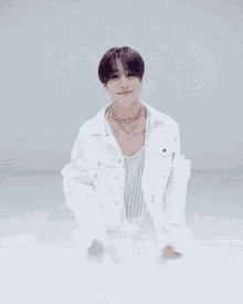 a man wearing a white jacket and a necklace is kneeling down