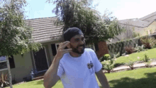a man with a beard is standing in front of a house talking on a cell phone