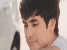 a close up of a young man 's face with his eyes closed and a white shirt on .