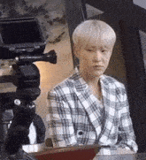 a young man in a plaid suit is sitting in front of a camera .