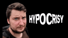 a man with a beard is standing in front of a black background with hypocrisy written on it