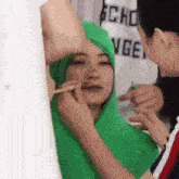 a man is applying makeup to a woman wearing a green hoodie