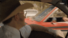 a man in a cowboy hat is driving a red car with the word max on the bottom