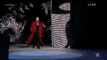 a man in a red coat is walking on a stage with the word live on the bottom