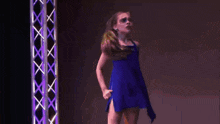 a young girl in a blue dress stands in front of a purple structure