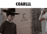 a man in a cowboy hat is standing in front of a brick wall with the word c block written on it