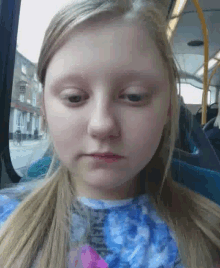a girl with long blonde hair is sitting on a bus and looking at the camera