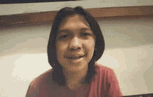 a young man with long hair is smiling and looking at the camera while wearing a red shirt .