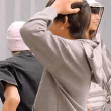 a woman in a gray hoodie is touching her hair while standing next to another woman .