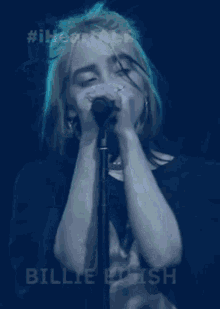 billie eilish is singing into a microphone on a stage with her eyes closed .