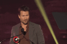 a man in a suit stands in front of a microphone holding a red trophy