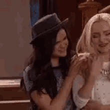 two women are sitting next to each other in a room and one of them is wearing a hat .