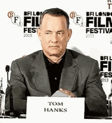 a man in a suit is sitting at a desk with a sign that says tom hanks