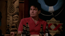 a man in a red shirt is holding a bottle of dos equis