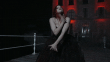 a woman in a black dress is dancing in front of a building with red lights