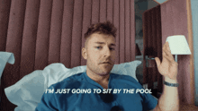 a man in a blue shirt is sitting in a bed with the words i 'm just going to sit by the pool below him