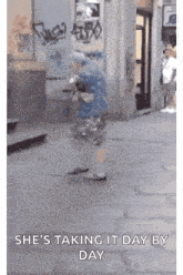 a person is walking down a street with the words `` she 's taking it day by day '' written on the sidewalk .