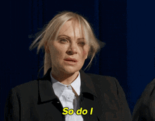 a woman in a suit says so do i in front of a blue curtain