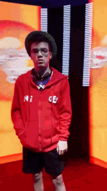 a man wearing a red nice hoodie is standing in front of a large screen .