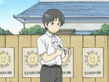 a boy stands in front of a fence with signs that say kamakura on them