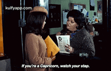 two women are talking to each other in a room and one of them is holding a newspaper .