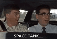 two men are sitting in the back seat of a car and one of them is saying `` space tank ... '' .
