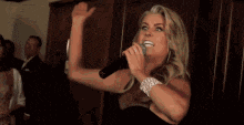 a woman in a black dress is singing into a microphone while standing in front of a crowd .