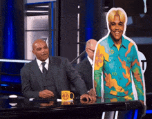 a man in a suit sits at a desk next to a yellow mug that says ' nba ' on it